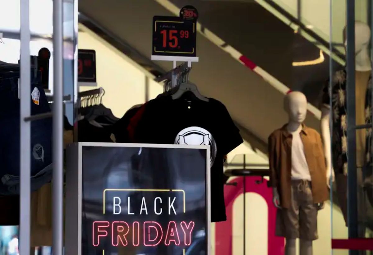 Placa de Black Friday em loja de roupas com camiseta preta, preço promocional e manequins ao fundo