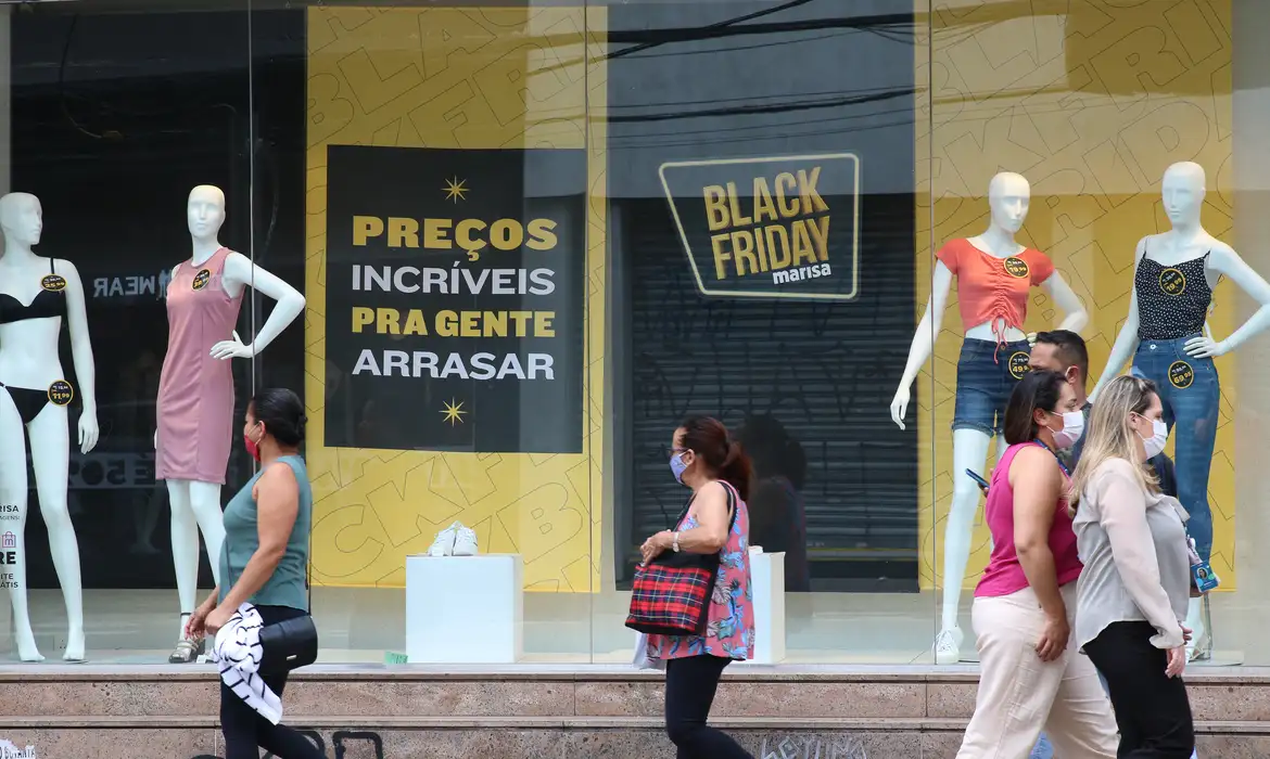 Como caçar promoção do jeito certo e identificar o falso desconto antes de comprar em 2026 2 Pessoas de máscara passam em frente a vitrine da Marisa com manequins e cartazes de Black Friday