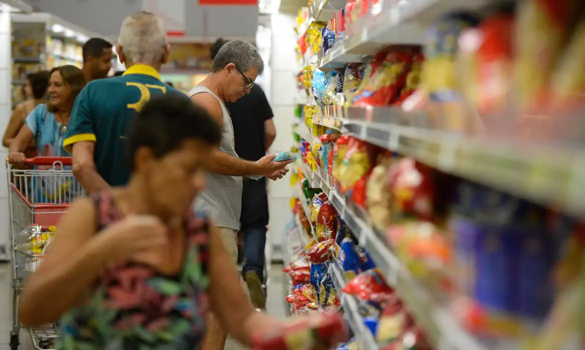 Como economizar dinheiro em 2026: 7 estratégias que cabem no seu dia a dia e funcionam de verdade 2 Pessoas adultas observam e escolhem produtos em prateleiras de supermercado cheio